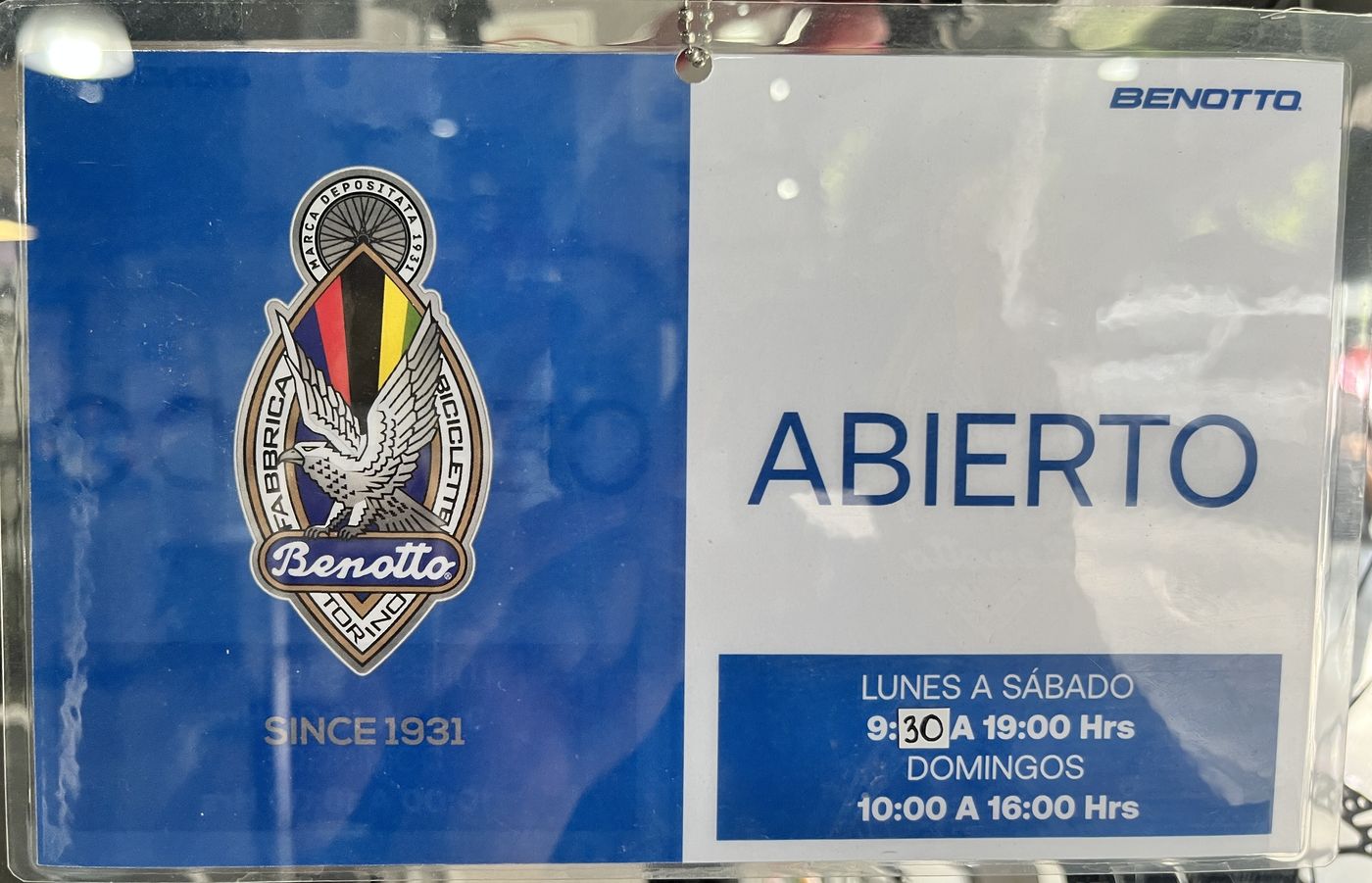 The opening-hours sign on a store door, with the crest used as decoration and the italic wordmark