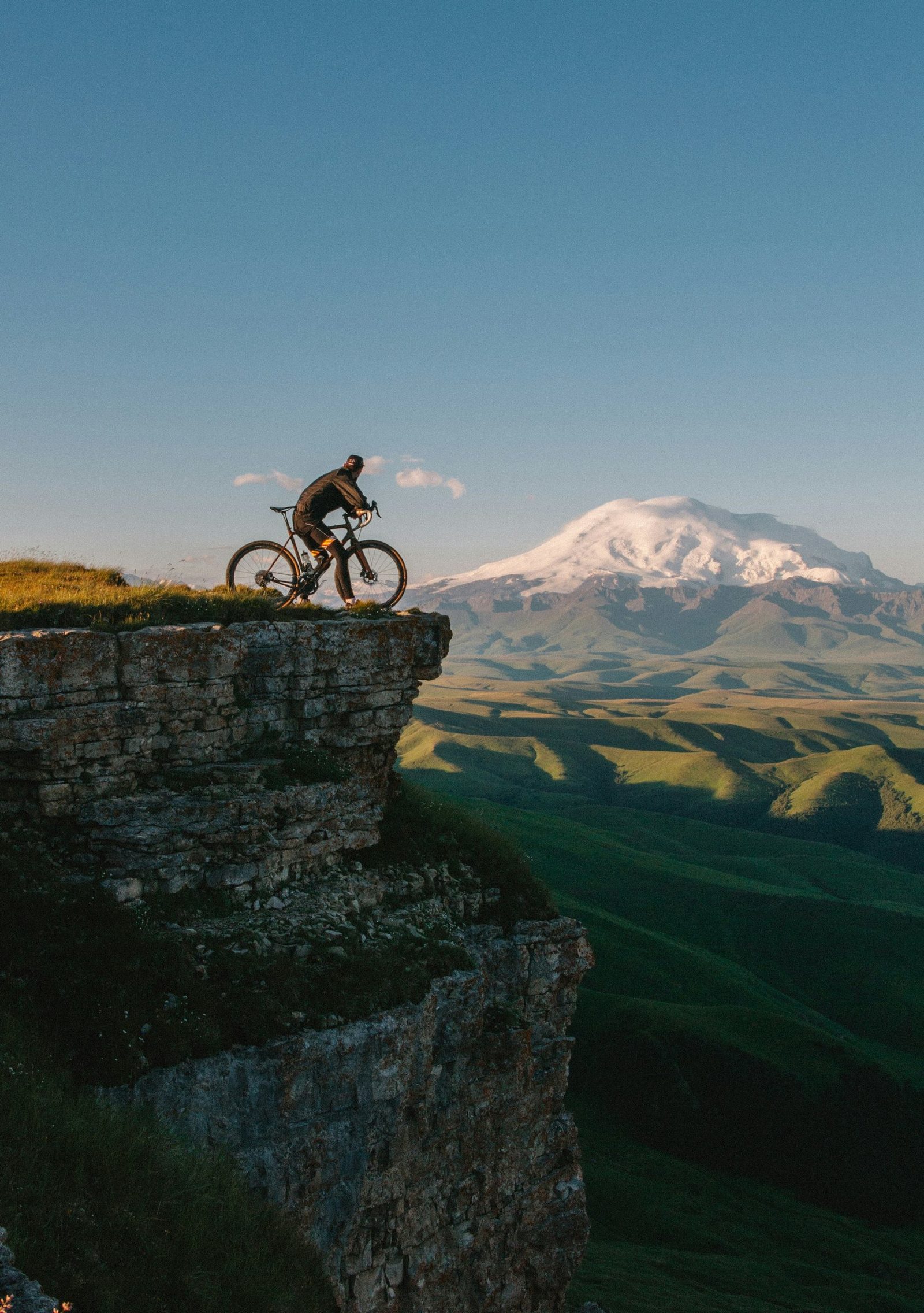 A mountain biker on a cliff edge facing a snow-capped volcano